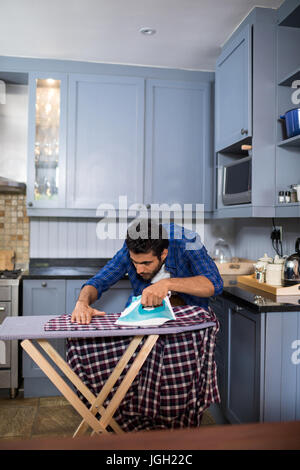 Uomo maglietta di stiratura a bordo mentre in piedi in cucina Foto Stock