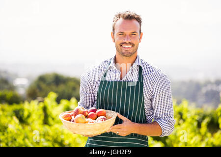 Ritratto di sorridente giovane azienda mela paniere contro sky sulla giornata di sole Foto Stock