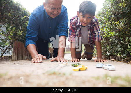 Ragazzo e nonno a giocare con modellini di auto in ginocchio sul marciapiede in cantiere Foto Stock