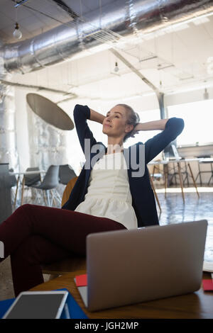 Riflessivo imprenditrice con le mani dietro la testa in un momento di relax a office Foto Stock