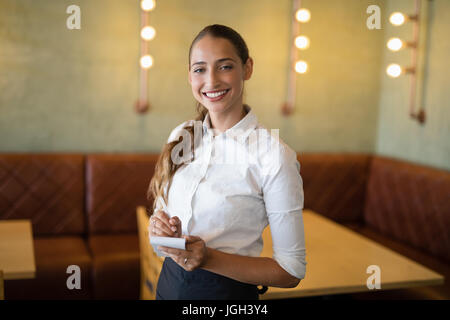 Ritratto di sorridente cameriera prendendo un ordine su notepad in bar Foto Stock