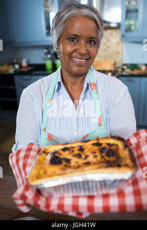 Close up ritratto di donna senior mostra cibo cotto mentre in piedi in cucina a casa Foto Stock