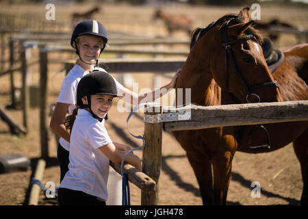 Ritratto di ragazze sorridenti in piedi vicino al marrone a cavallo al ranch Foto Stock