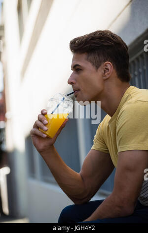 Vista laterale del giovane uomo di bere succo di frutta durante la seduta da parete in città Foto Stock