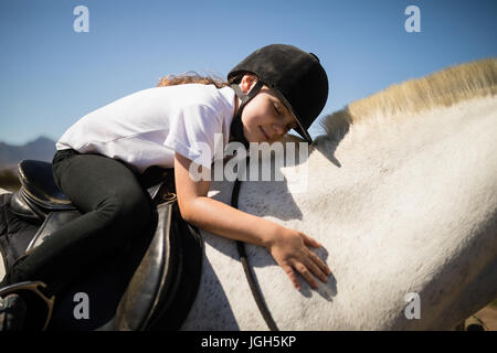 Ragazza sorridente che abbraccia il cavallo bianco nel ranch in una giornata di sole Foto Stock