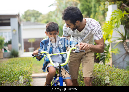 Uomo che assiste il figlio per il ciclismo in cantiere Foto Stock