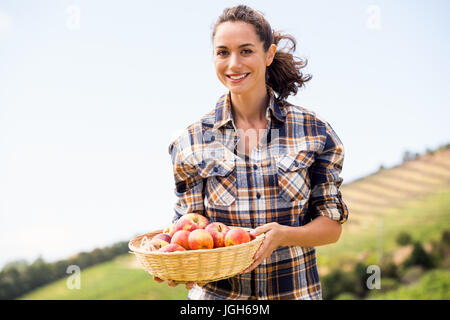 Ritratto di sorridente giovane donna azienda mela paniere presso l'azienda Foto Stock