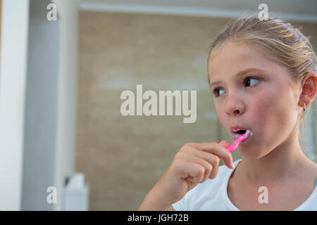 Close up di una ragazza che guarda lontano durante la spazzolatura di denti in bagno Foto Stock