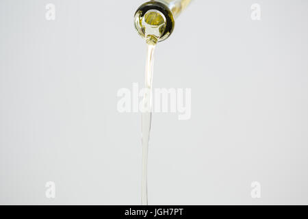 Olio di olive verdi versata da bottiglia contro uno sfondo bianco Foto Stock