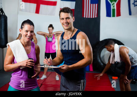 Ritratto di giovane maschio e femmina atleti discutendo con appunti mentre in piedi in studio fitness Foto Stock