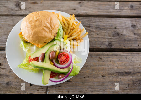 Vista aerea del cheeseburger con insalata e patatine fritte servite nella piastra sulla tavola Foto Stock