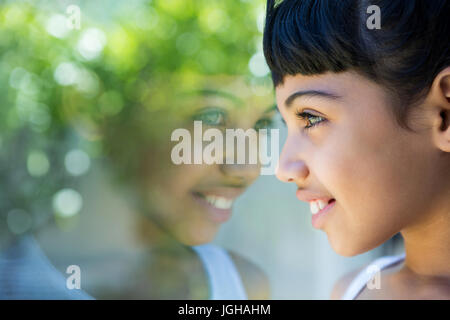 Close-up della ragazza sorridente guardando attraverso la finestrella a casa Foto Stock