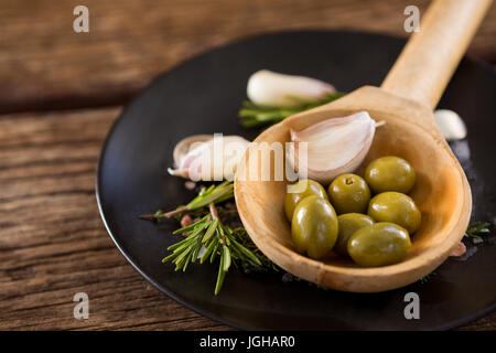 Close-up di olive verdi, rosmarino e il mestolo di legno sul tavolo Foto Stock