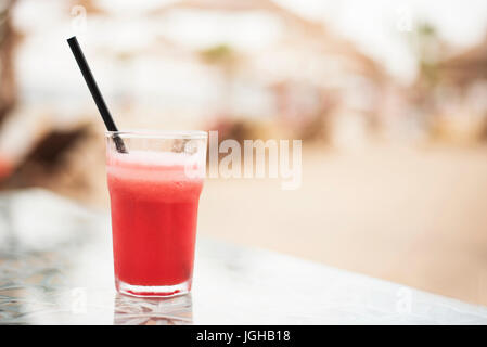 Cocktail di rosso e di anguria fresco su un tavolo vicino. Sullo sfondo sfocato ombrelloni sulla spiaggia. Sun, haze, bagliore Foto Stock