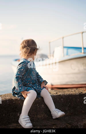 Una bambina con un vestito blu sulla banchina che guarda al mare. Barca in background. Filtro, la colorazione Foto Stock