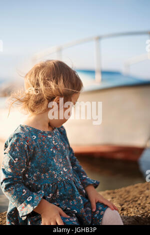 Una bambina con un vestito blu sulla banchina che guarda al mare. Barca in background. Colorazione vintage Foto Stock