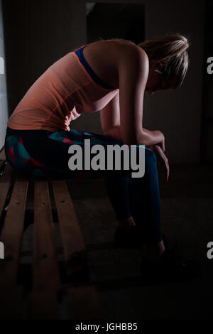 Triste donna rilassante sul banco di lavoro in studio fitness Foto Stock