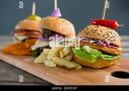 Varie gli hamburger con patatine fritte sul tagliere al tavolo contro la parete Foto Stock