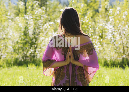 Vista posteriore della donna facendo retromarcia posa di preghiera nella foresta in una giornata di sole Foto Stock