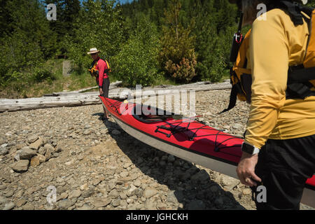 Matura portante kayak mentre in piedi sulle rocce sul lungolago Foto Stock