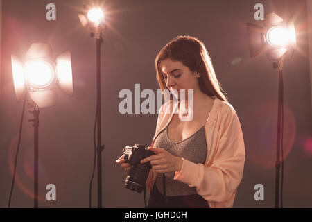 Fotografo femmina tenere la fotocamera illuminato da luci stroboscopiche allo studio Foto Stock