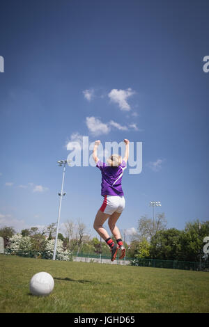 Vista posteriore per tutta la lunghezza della femmina di giocatore di calcio di saltare sul campo contro sky Foto Stock