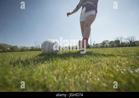 Sezione bassa della donna che giocano a calcio sul campo contro il cielo durante la giornata di sole Foto Stock