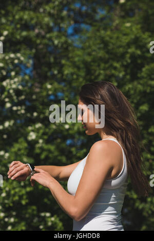 Donna che utilizza smartwatch in park in una giornata di sole Foto Stock