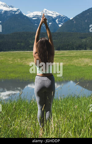 Vista posteriore della donna facendo esercizio di stiramento su erba verde Foto Stock