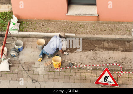 Muratore al lavoro la posa di blocchi di pietra di pavimentazione. Foto Stock