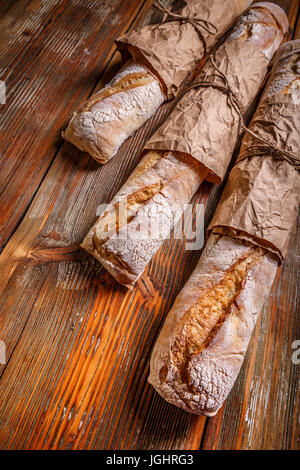 Fresca baguette francese su una tavola di legno avvolti in carta kraft Foto Stock