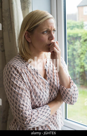 Triste la donna che soffre di agorafobia guardando fuori della finestra Foto Stock