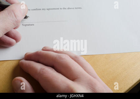 Stretta di mano maschio firma 'Signature' porzione su linea punteggiata di bianco di un documento legale con cartuccia pen pennino, mentre l'altra mano si appoggia sulla luce Foto Stock