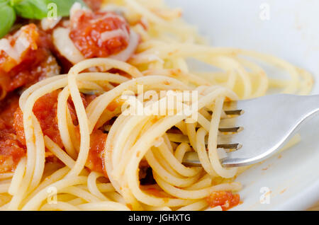 Una ciotola di pasta, la salsa di pomodoro e le foglie di basilico con formaggio. Close-up di avvolgimento a forcella e sollevamento di spaghetti in primo piano. Foto Stock