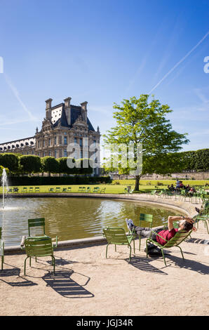 Il giardino delle Tuileries a Parigi, Francia, da una mattina di sole con un uomo in appoggio su un prato di metallo sedia in prossimità di un bacino di acqua e Palazzo del Louvre. Foto Stock