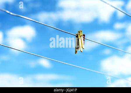 Tre colorati abiti in plastica pioli su una famiglia di linea di lavaggio con cielo blu e bianco delle nuvole di estate in background Foto Stock