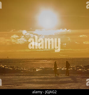 Camminare in inverno lungo il mare. Caldo sole del tramonto e sagome di persone Foto Stock