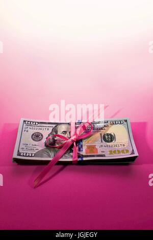 Pila di nuovo Hundred Dollar Bills contanti 100 USD soldi americani su un sfondo rosa tenute insieme con il nastro rosa legato in un arco Foto Stock