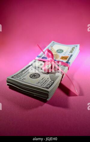 Pila di nuovo Hundred Dollar Bills contanti 100 USD soldi americani su un sfondo rosa tenute insieme con il nastro rosa legato in un arco Foto Stock