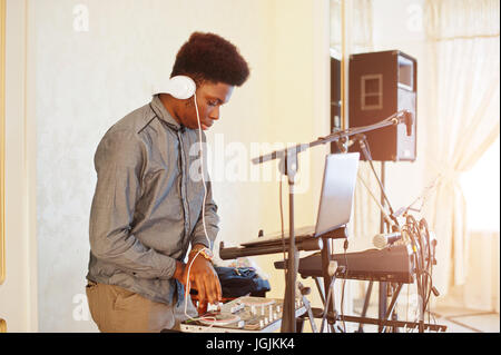African American dj in enormi cuffie bianche creazione di musica su pannello di miscelazione. Foto Stock