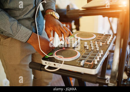 African American dj in enormi cuffie bianche creazione di musica su pannello di miscelazione. Foto Stock