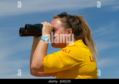 Bagnino femminile con binocolo su Crosby Beach, Merseyside, Regno Unito. Regno Unito Meteo. Giornata di sole sull'estuario del Mersey con temperature elevate negli anni '20 e viste chiare sul fiume Mersey e sul mare irlandese. Credito; MediaWorldImages/AlamyLiveNews Foto Stock