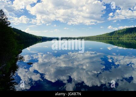 Nuvole e alberi si riflette ancora in un lago Foto Stock