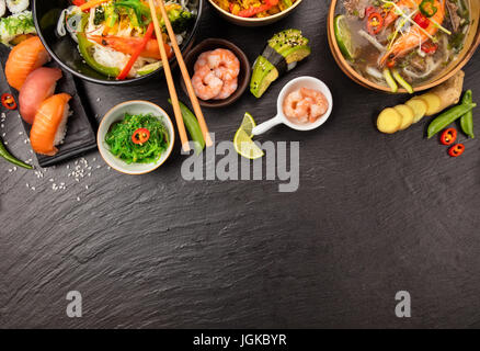 Cibo asiatico tabella con vari tipi di cucina cinese e, tagliatelle, pollo, zuppa di gamberi, riso sushi e molti altri. Servita sulla pietra nera tabella, vista dall'alto. Foto Stock