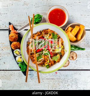 Asian pollo e curry di gamberi con riso e pezzi di sushi, vista dall'alto, servita su vecchie tavole di legno. Foto Stock