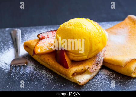 Crepes fiiled con marmellata, fette di pesche e gelato scoop su top con zucchero a velo, frutti dolci dessert Foto Stock