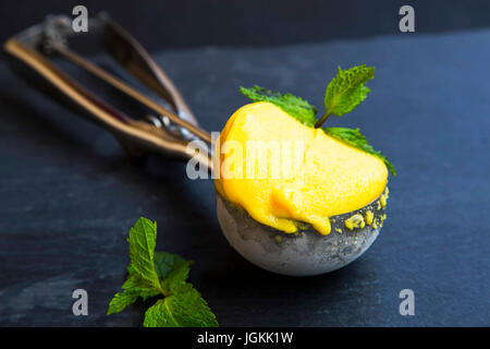 Il sorbetto di mango, summerish dessert in uno scoop decorato con foglie di menta, primo piano Foto Stock