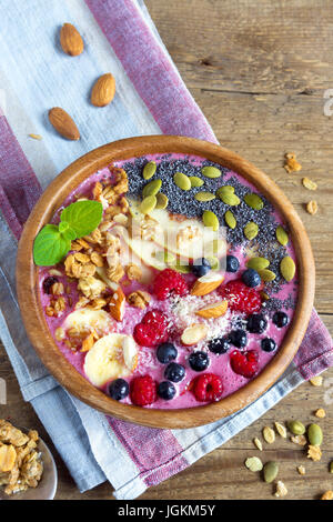 Una sana colazione ciotola smoothie guarnita con frutta, bacche e i semi di più rustico sfondo di legno con spazio di copia Foto Stock