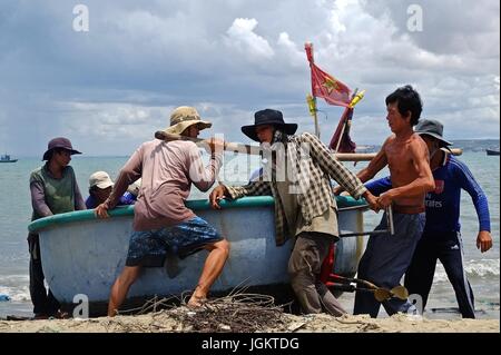 I pescatori vietnamiti tirare una piccola barca sulla spiaggia di Mui Ne, Vietnam Foto Stock