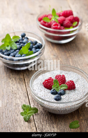 Budino di chia con lamponi e mirtilli in una ciotola di vetro, frutti di bosco freschi sul vecchio sfondo di legno Foto Stock